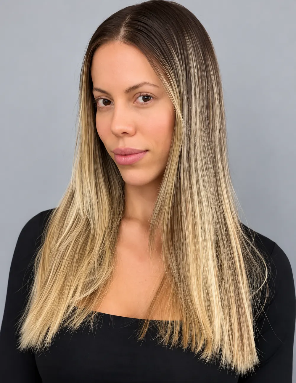 Mulher com cabelo longo liso, raiz castanha e comprimento loiro acinzentado, usando blusa preta sobre fundo cinza